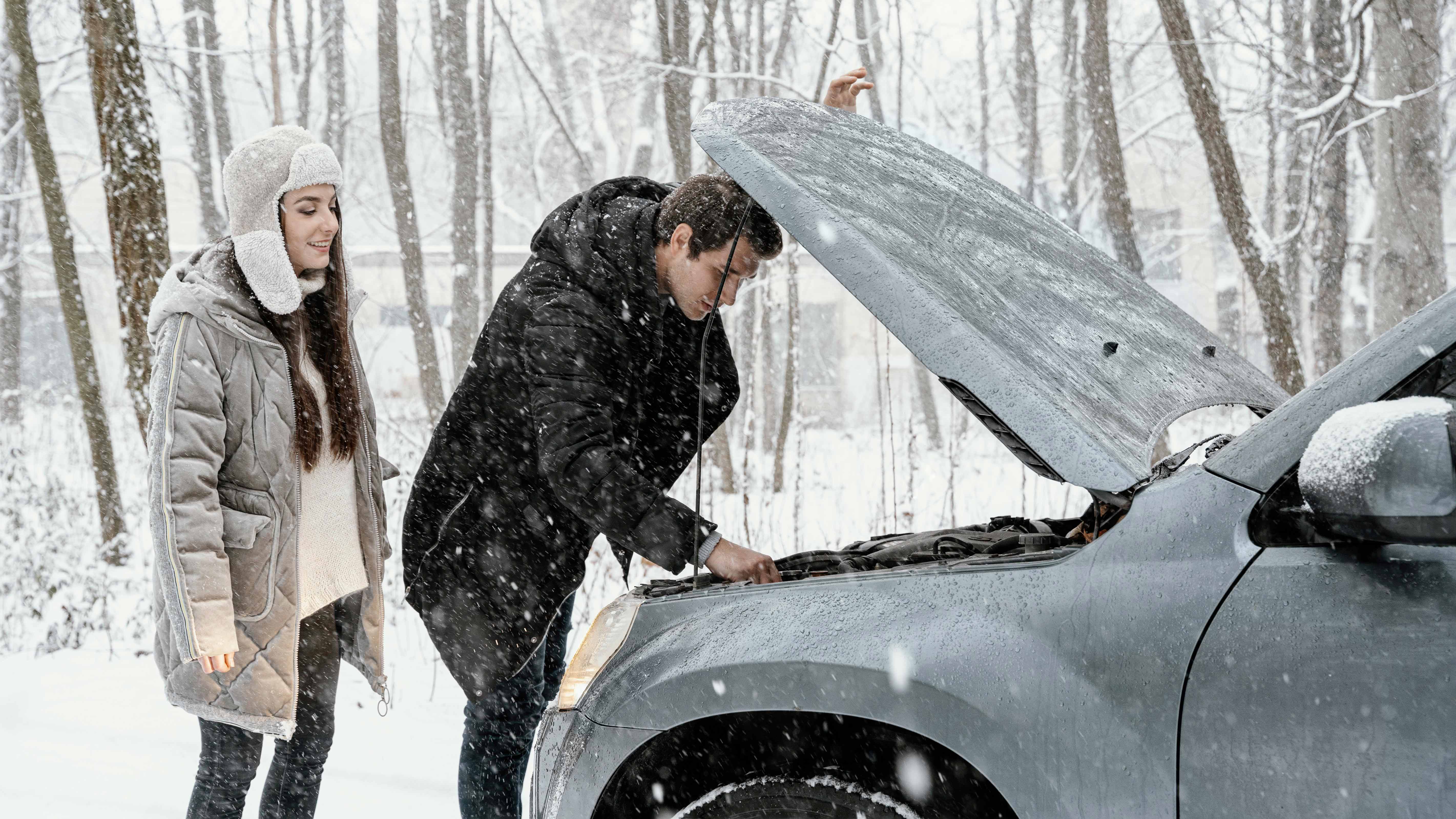 žena a muž stojaci pred otvorenou kapotou pokazeného auta v zime